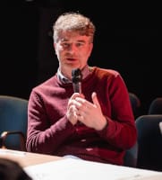 Na zdjęciu dr hab. Rafał Włodarczyk, w bordowym swetrze, mówi do mikrofonu, siedząc przy stole.