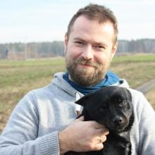 Dr Kamil Pietrowiak trzyma czarnego psa na tle pola, ekspert w badaniach nad życiem osób niewidomych.