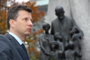 Na zdjęciu dr Marek Michalak w garniturze, na tle pomnika przedstawiającego rodzinę.