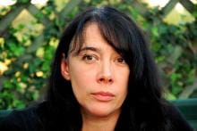 Na zdjęciu prof. dr hab. Iwona Chrzanowska z długimi ciemnymi włosami, siedzi na tle zielonego ogrodzenia.