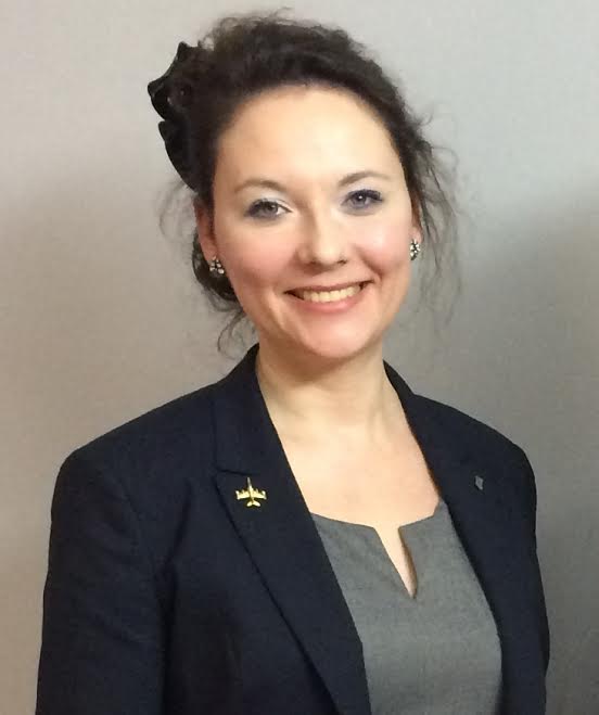 Na zdjęciu prof. nadzw. dr hab. Anna Odwrąż-Coates w ciemnej marynarce i szarej bluzce, uśmiechnięta na jasnym tle.